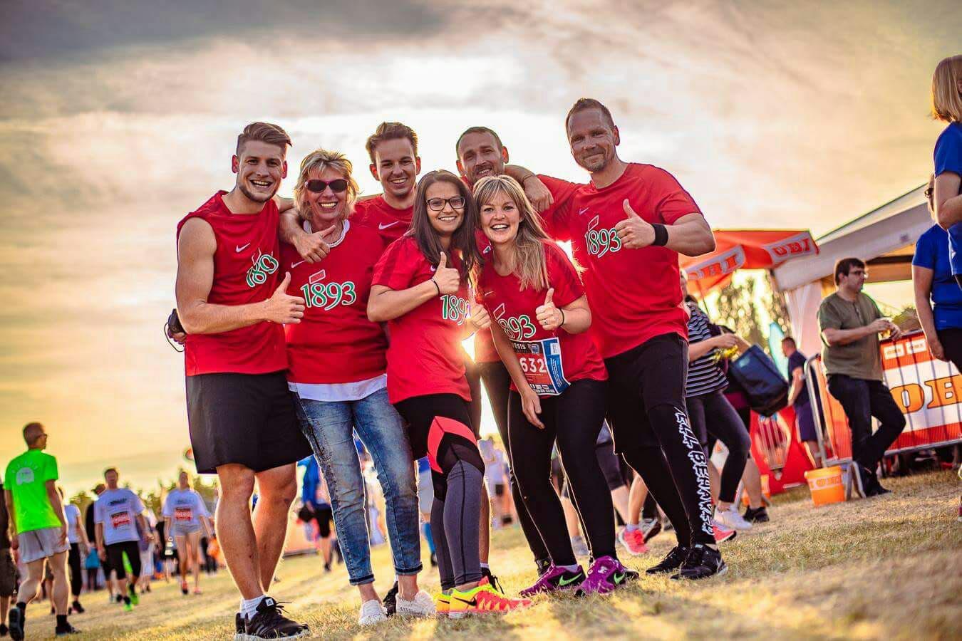 Mitarbeiter der 1893 tragen rote Lauftrikots und posieren lachend in die Kamera