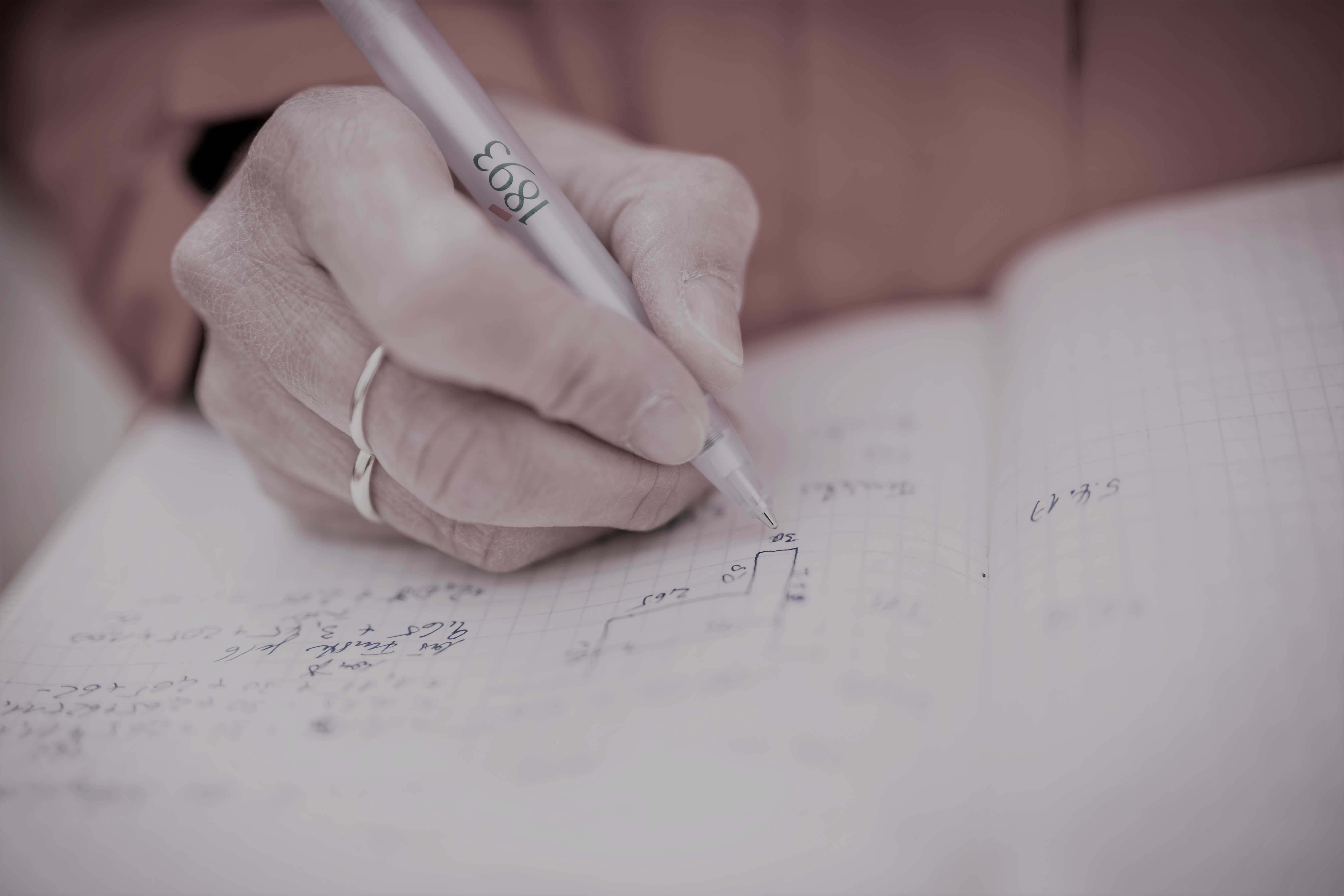 Hand mit Ring hält Stift und schreibt mathematische Formeln und Diagramme in ein Notizbuch