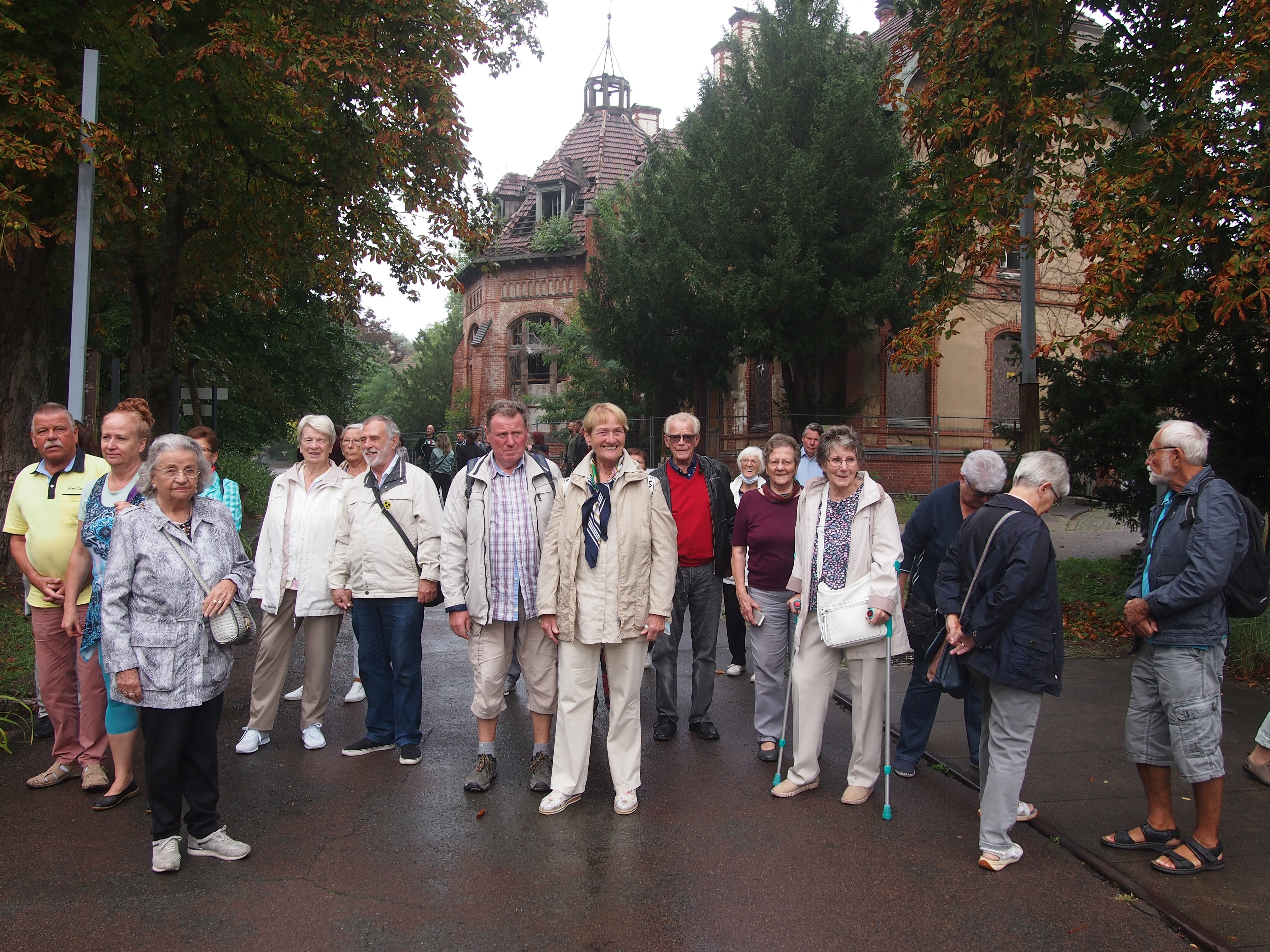 Gruppe älterer Menschen steht auf einem Gehweg vor einem historischen Gebäude in Beelitz, umgeben von Bäumen
