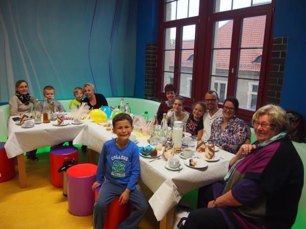 Kinder und Erwachsene sitzen an einer gedeckten Tafel und gucken lachend in die Kamera