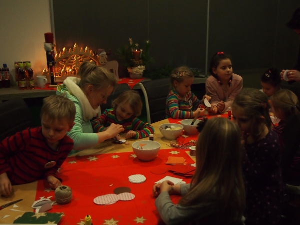 Mehrere Kinder sitzen an einem Tisch mit weihnachtlicher Dekoration und basteln.