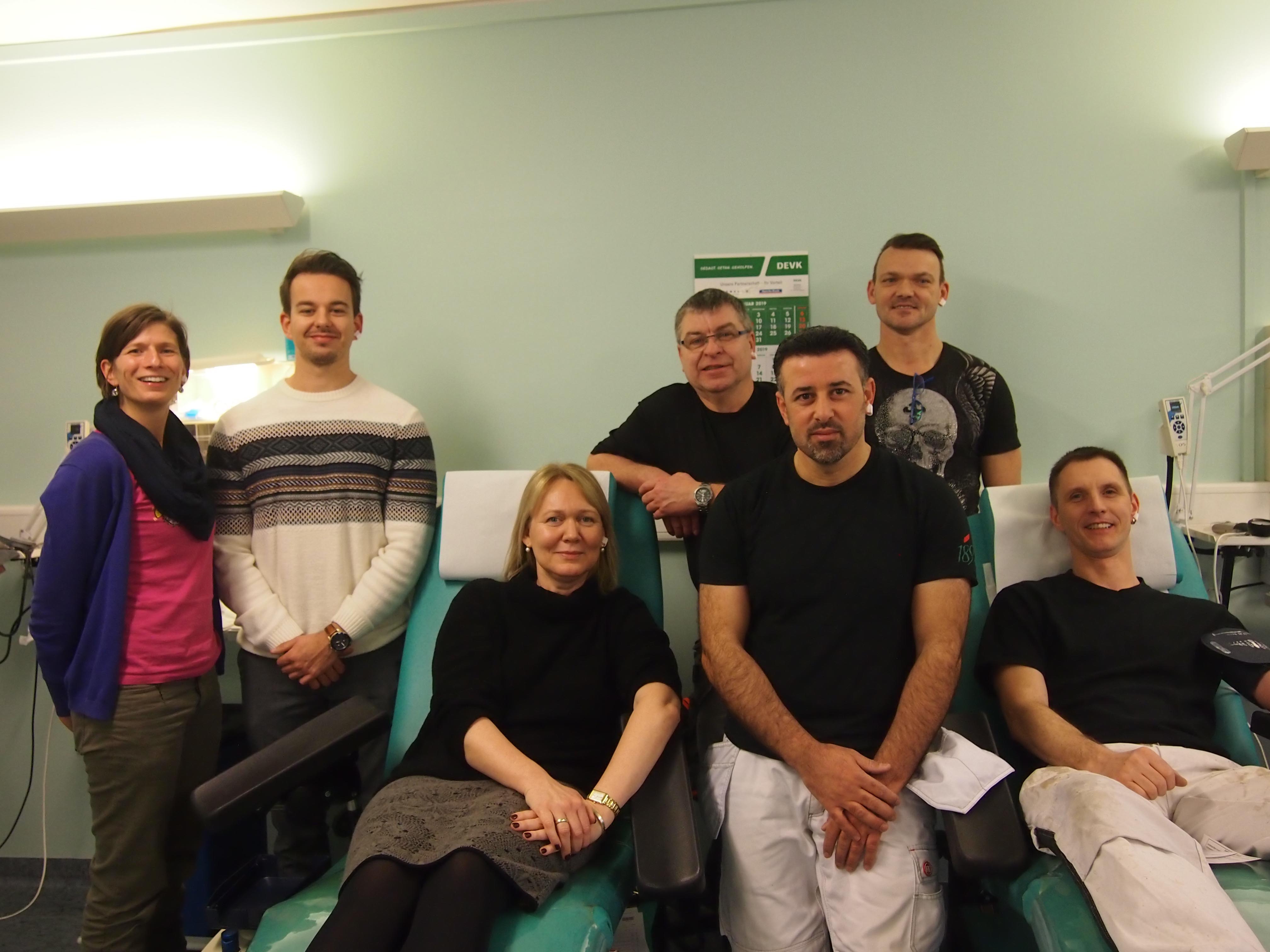 Mitarbeiter der 1893 eG stehen in einem Blutspende-Raum, zwei Menschen sitzen auf einer Liege