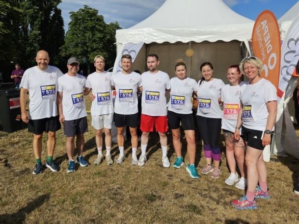 Neun Läufer in weißen T-Shirts mit Startnummern stehen vor einem weißen Zelt bei der Firmenstaffel 2025