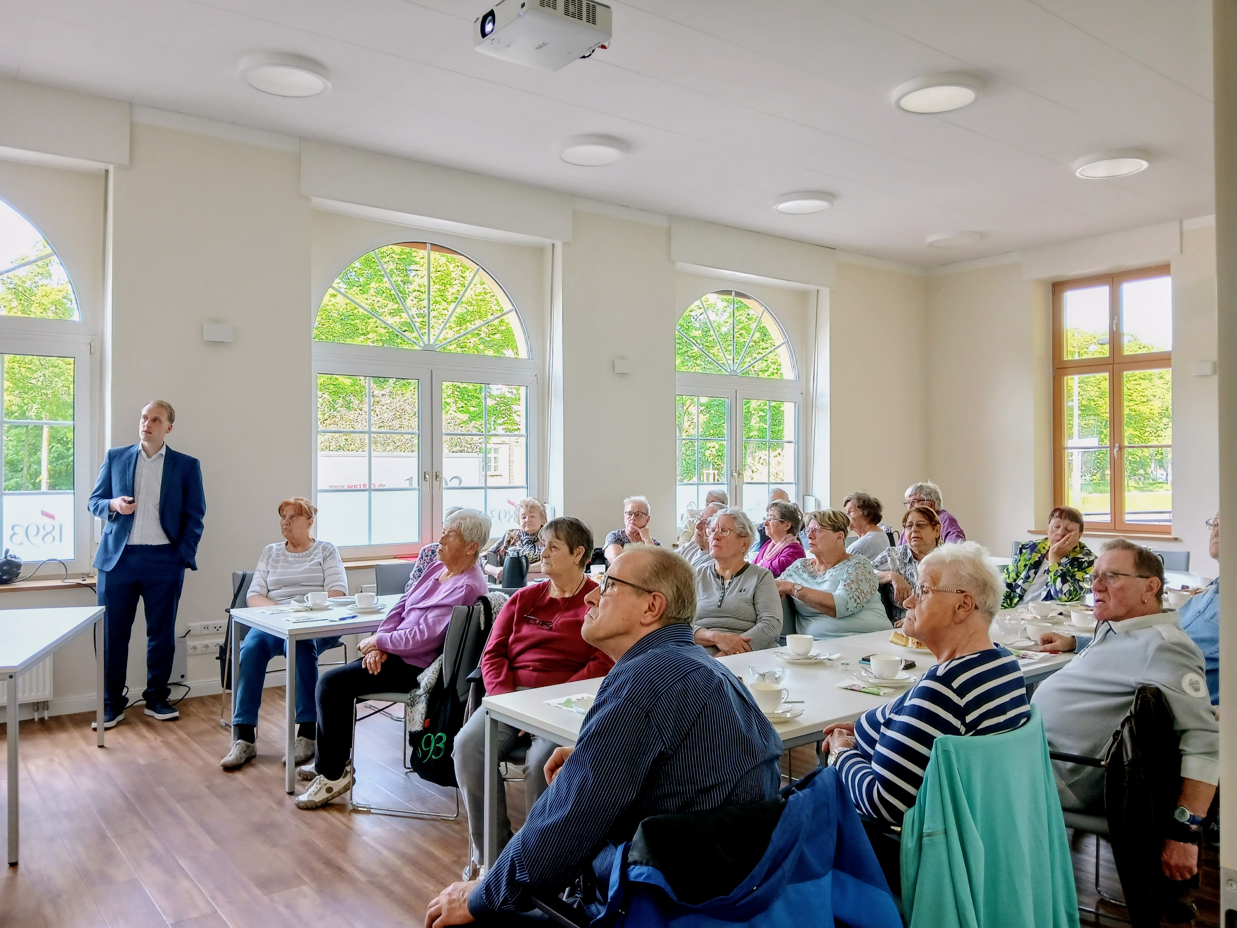 Gruppe von Menschen sitzt am Tisch und guckt auf Beamer-Show