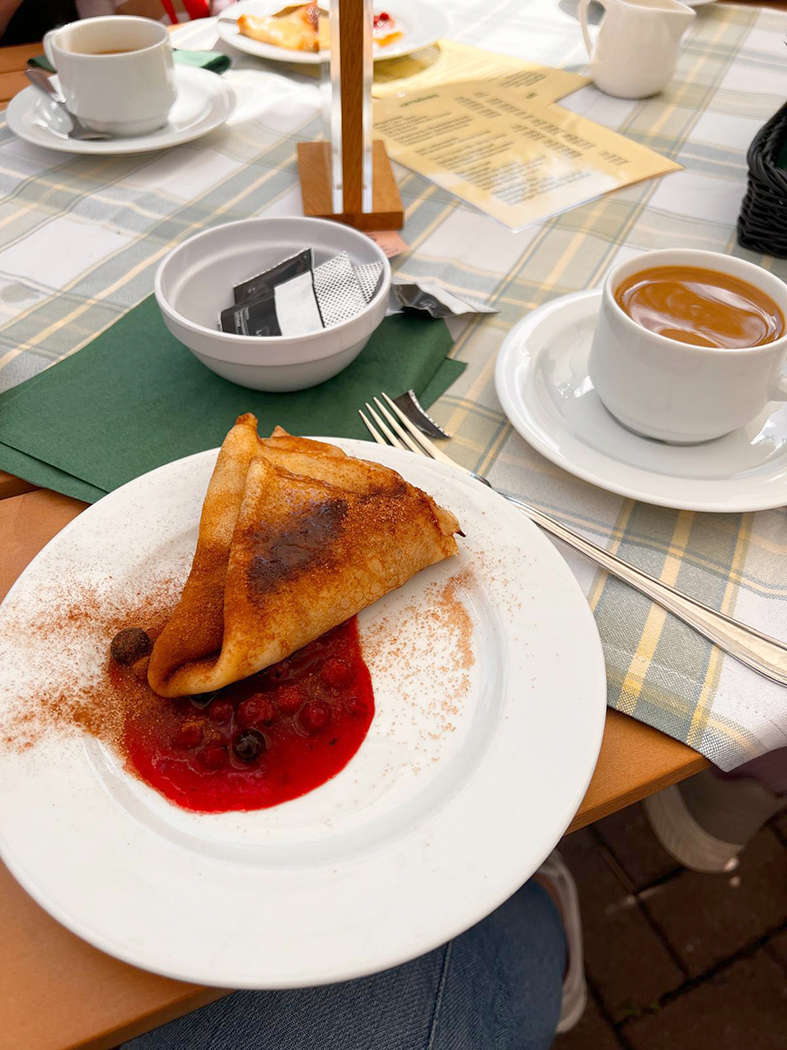 Ein Plins mit Beerensoße und eine Tasse Kaffee stehen auf einem gedeckten Tisch im Restaurant.